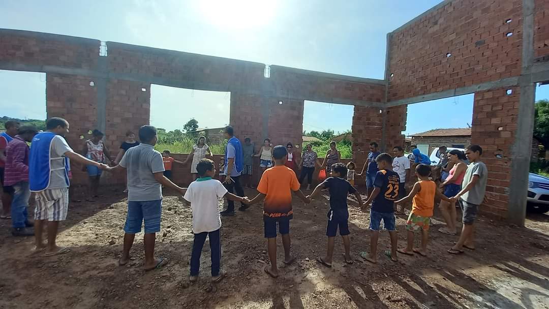 Voluntários e moradores de mãos dadas em oração no canteiro de obras de uma nova casa em Vargem Grande
